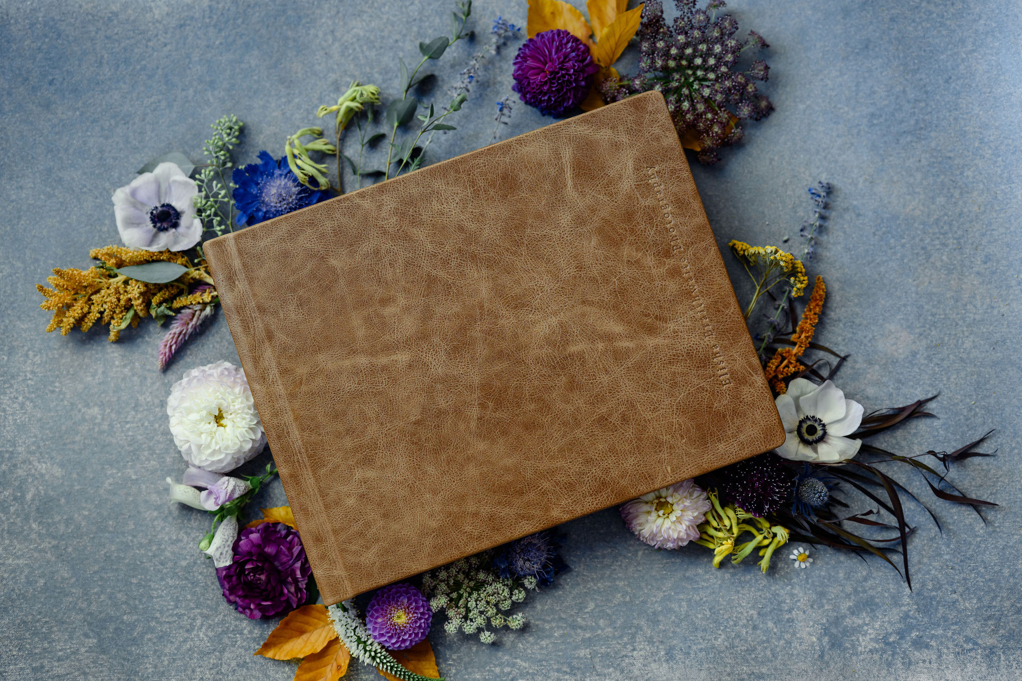 A leather bound photo album surrounded by flowers.