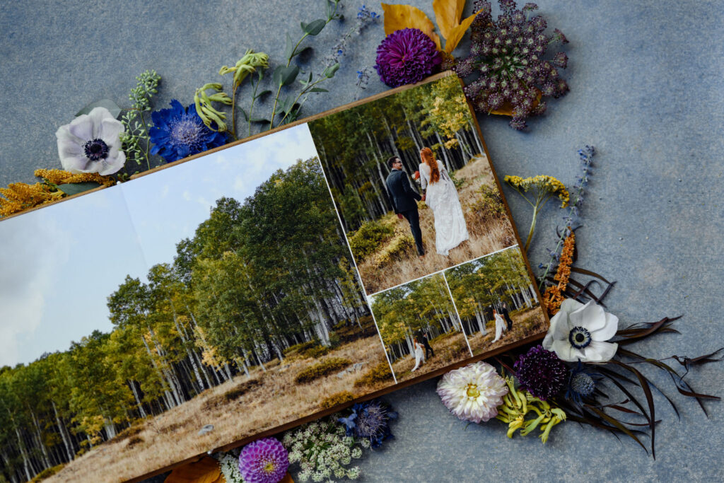 A flat lay photo album, surrounded by flowers, of a colorful fall scene where newlywed lovers walk through a field.