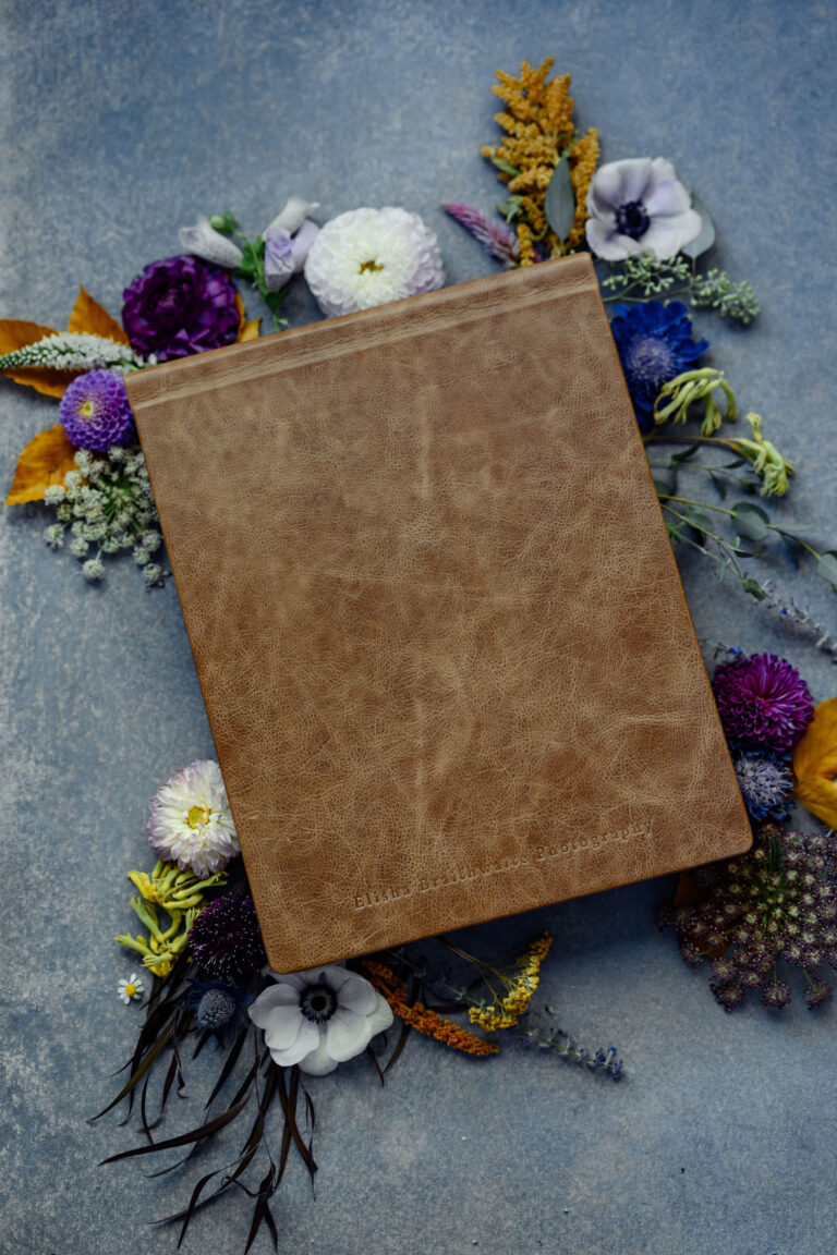 A brown leather photo album surrounded by flowers.