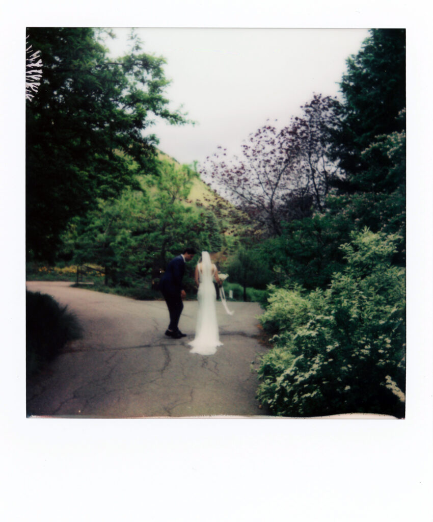 A Polaroid of a couple walking through a garden in their wedding attire.